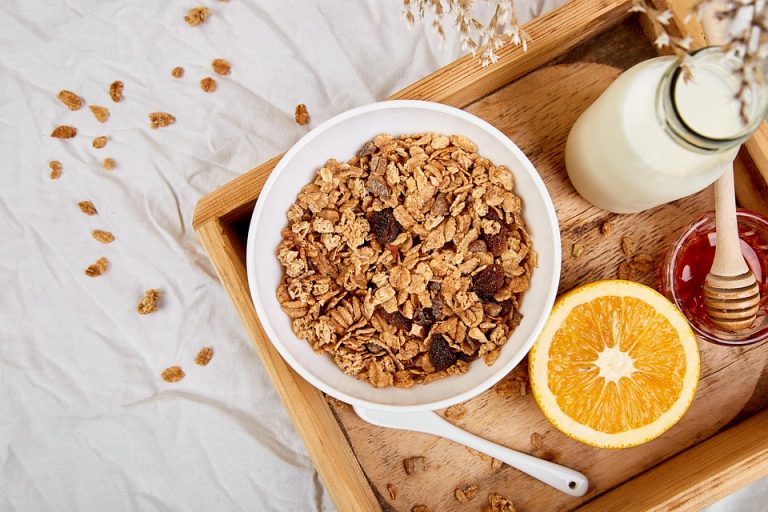 Bowl of granola with milk, orange, and honey on a wooden tray.