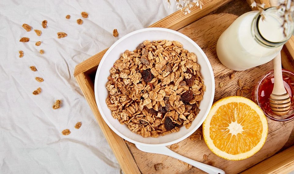 Bowl of granola with milk, orange, and honey on a wooden tray.