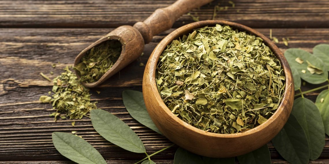 Dried moringa leaves in a wooden bowl on a rustic table.