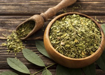 Dried moringa leaves in a wooden bowl on a rustic table.