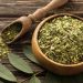 Dried moringa leaves in a wooden bowl on a rustic table.