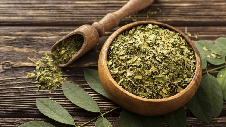 Dried moringa leaves in a wooden bowl on a rustic table.