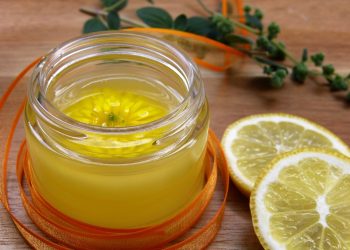Jar of lemon balm cream with sliced lemons on a wooden table.