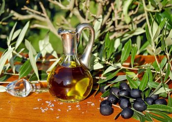 Olive oil in a glass jug with fresh olives on a wooden table.