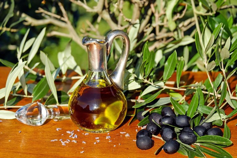Olive oil in a glass jug with fresh olives on a wooden table.