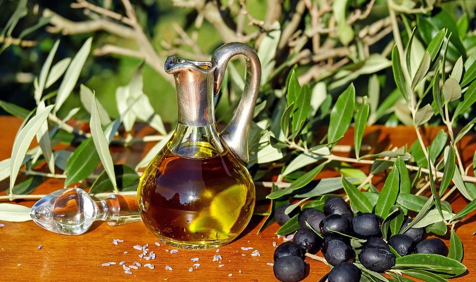 Olive oil in a glass jug with fresh olives on a wooden table.