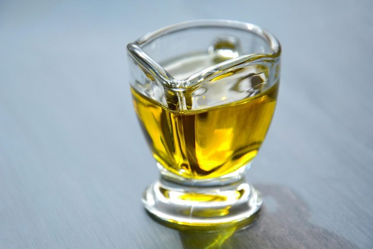 Golden olive oil in a glass container on a table.