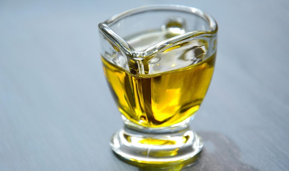 Golden olive oil in a glass container on a table.
