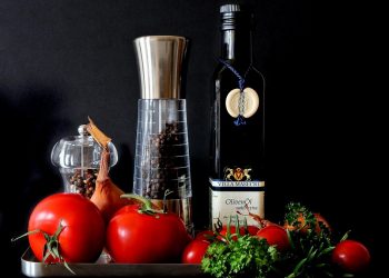 Fresh vegetables and olive oil with pepper mills displayed attractively.