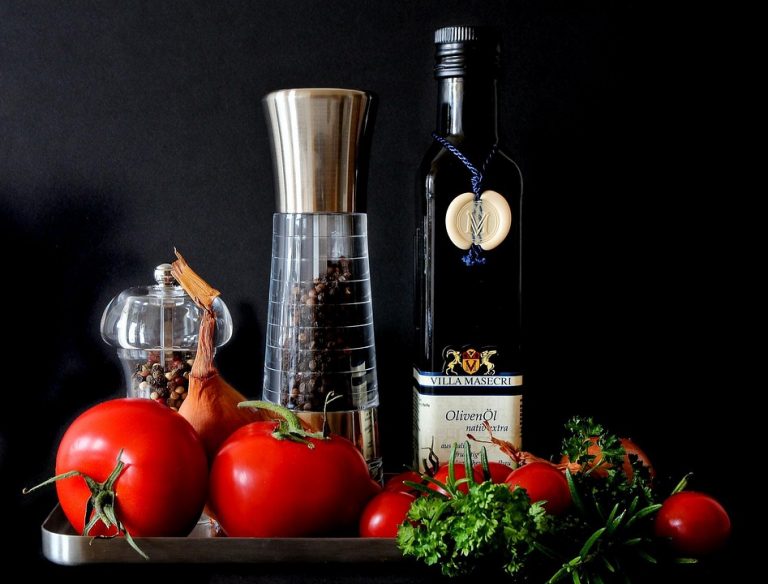 Fresh vegetables and olive oil with pepper mills displayed attractively.