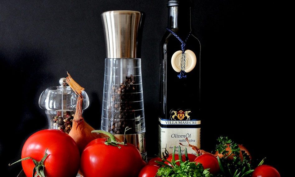 Fresh vegetables and olive oil with pepper mills displayed attractively.