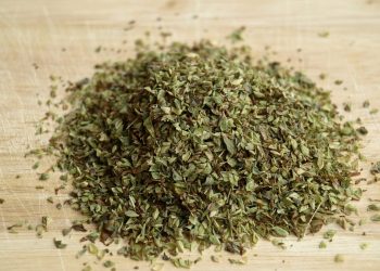 Dried oregano leaves on a wooden chopping board.