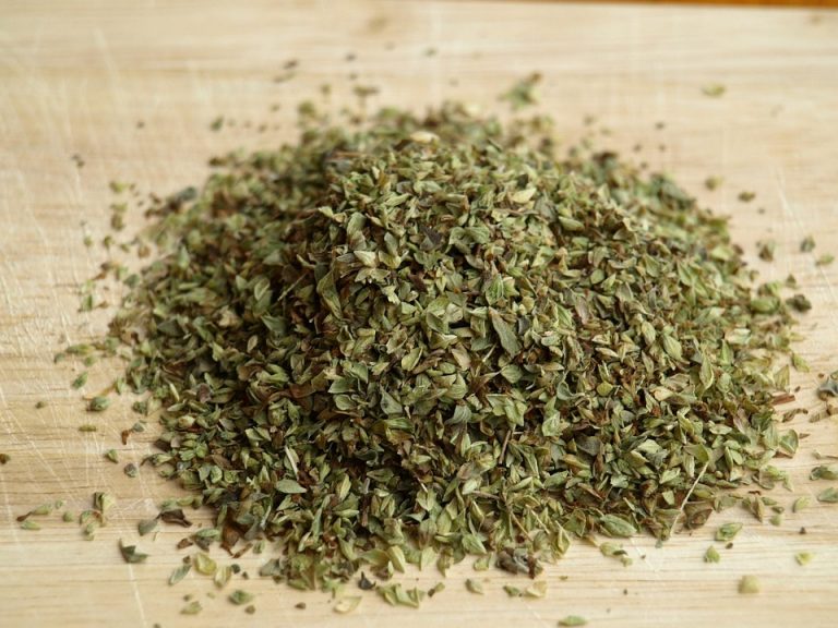 Dried oregano leaves on a wooden chopping board.