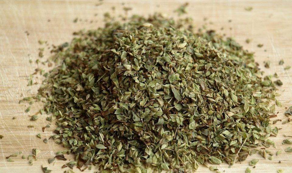 Dried oregano leaves on a wooden chopping board.
