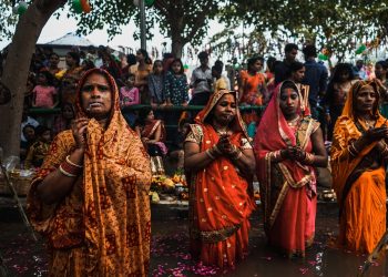 Women participating in a traditional prayer ceremony during a vibrant festival.
