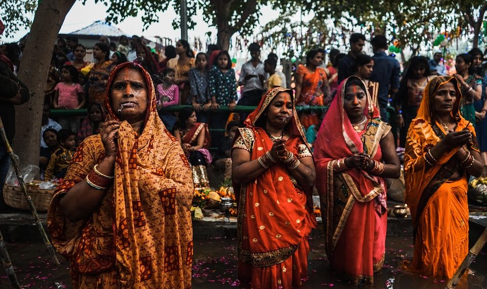 Women participating in a traditional prayer ceremony during a vibrant festival.