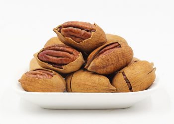 Pecans in shells stacked on a white plate.