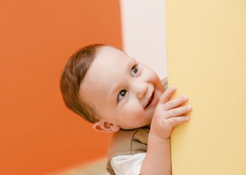 Toddler smiling while peeking around a yellow wall.