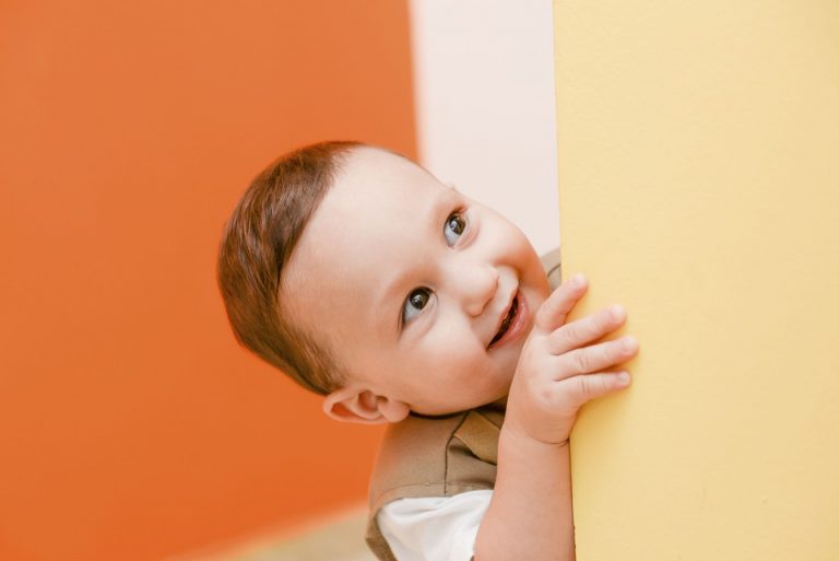 Toddler smiling while peeking around a yellow wall.
