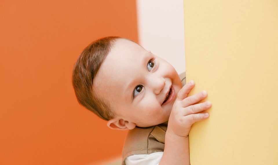 Toddler smiling while peeking around a yellow wall.