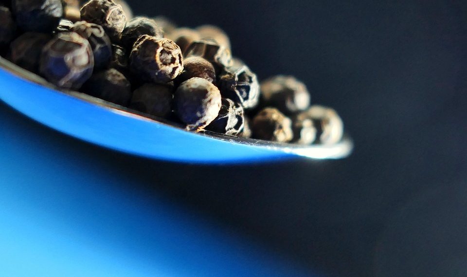 Black peppercorns on a spoon.