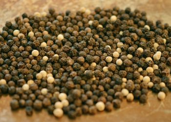 Black and white peppercorns scattered on a wooden surface.