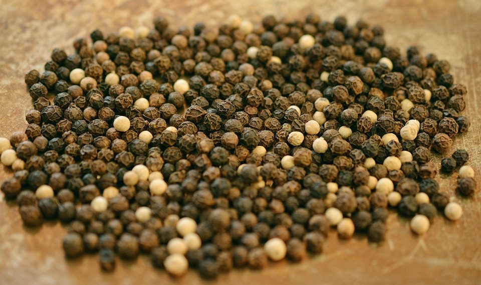 Black and white peppercorns scattered on a wooden surface.