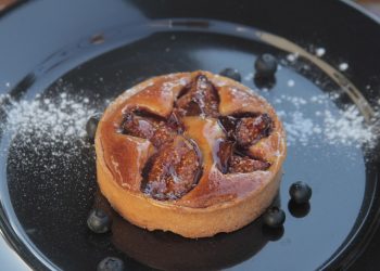 Fig tart on a black plate with scattered blueberries.