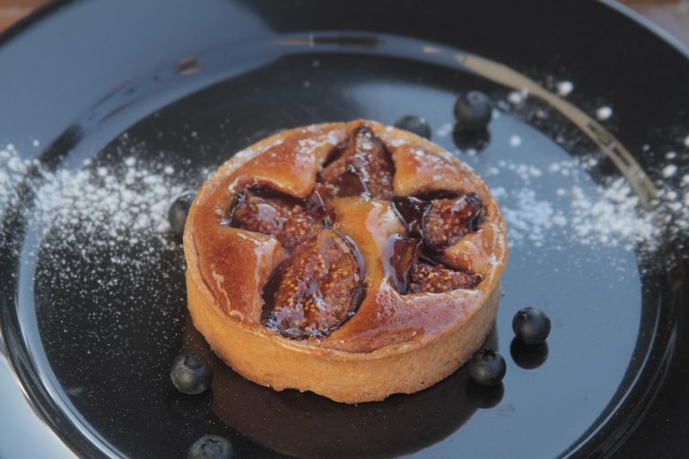 Fig tart on a black plate with scattered blueberries.