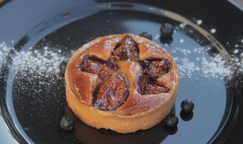 Fig tart on a black plate with scattered blueberries.