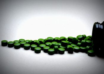 Green spirulina tablets spilled from black container