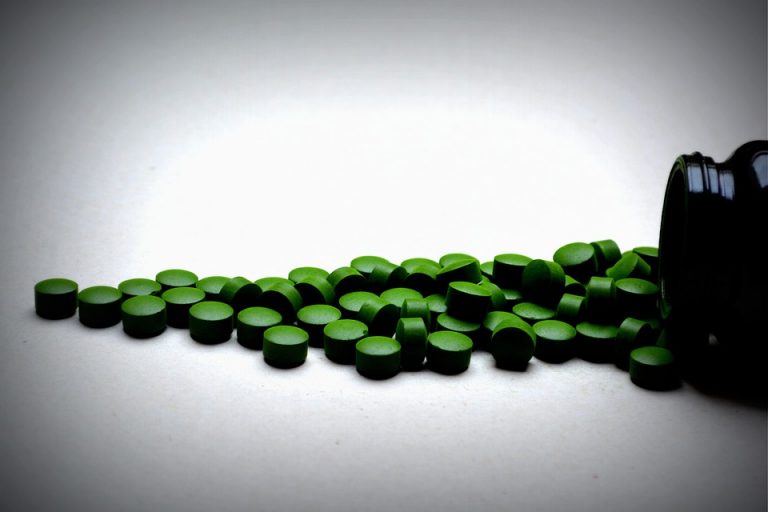 Green spirulina tablets spilled from black container