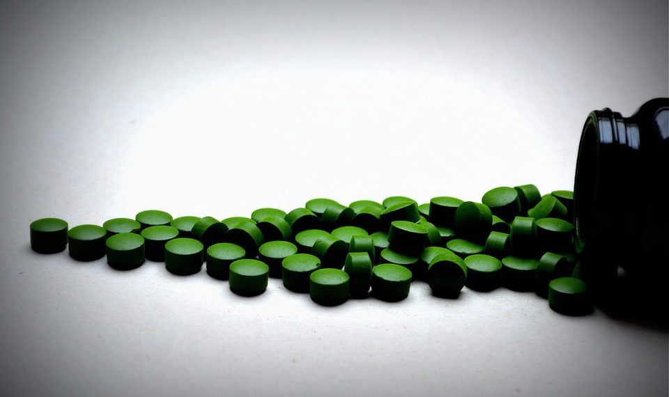 Green spirulina tablets spilled from black container