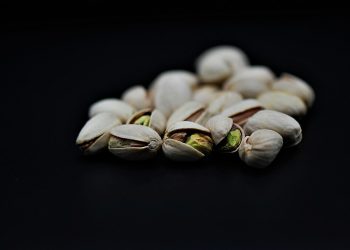 Pistachios against a black background, nuts partially open.