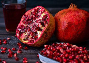 Fresh pomegranate and juice with seeds on dark table.