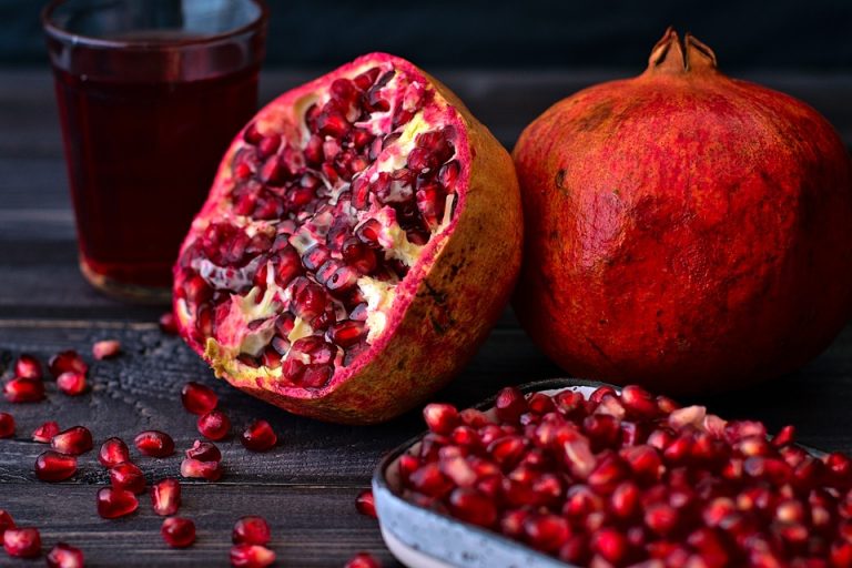 Fresh pomegranate and juice with seeds on dark table.