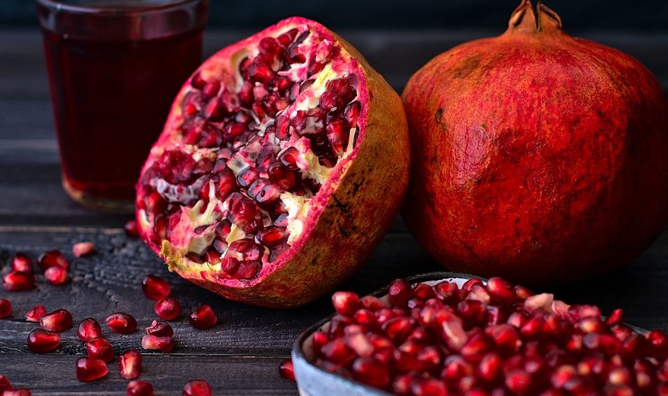 Fresh pomegranate and juice with seeds on dark table.