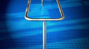 Stainless steel pool handrail over textured blue swimming pool cover.
