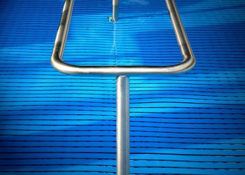 Stainless steel pool handrail over textured blue swimming pool cover.