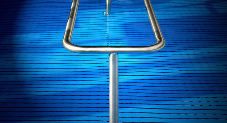 Stainless steel pool handrail over textured blue swimming pool cover.