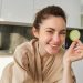 Woman smiling with cucumber slice in kitchen.