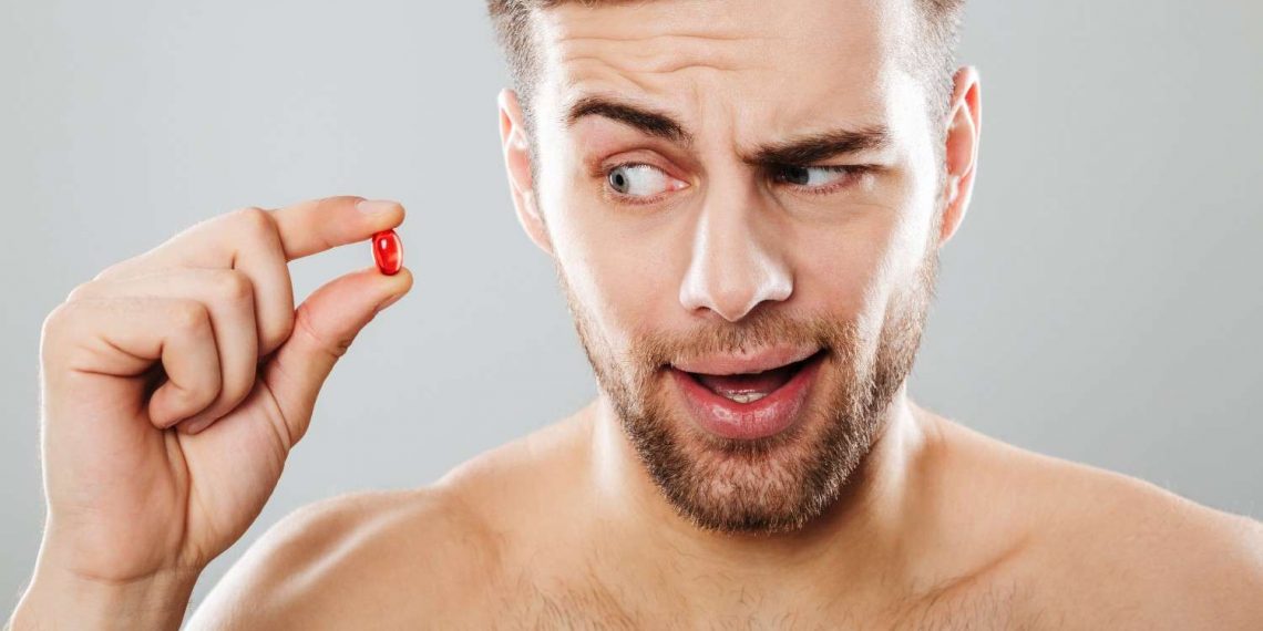 Man holding a red pill with a curious expression.