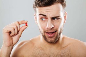 Man holding a red pill with a curious expression.
