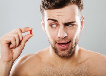 Man holding a red pill with a curious expression.
