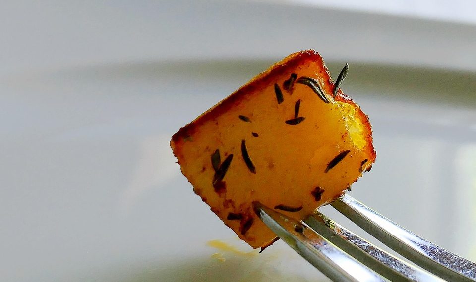 Roasted potato cube with herbs on a fork.