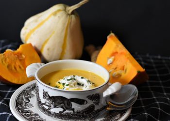Creamy pumpkin soup in a decorative bowl with fresh pumpkins.