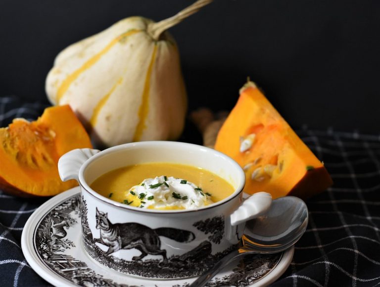Creamy pumpkin soup in a decorative bowl with fresh pumpkins.
