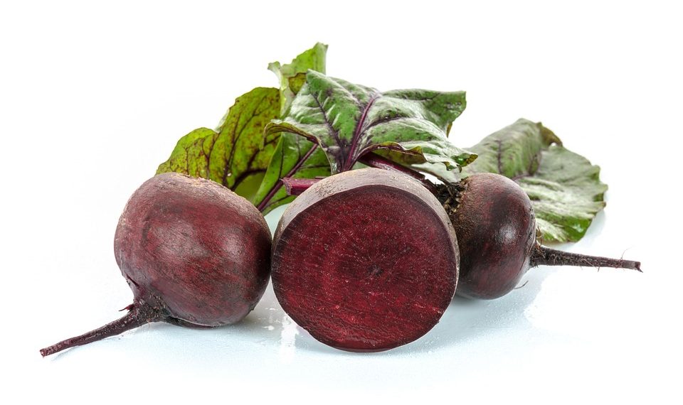 Whole and sliced beets with leaves on a white background.