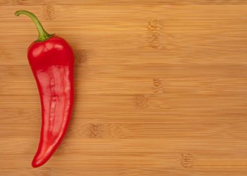 Red chili pepper on wooden cutting board.