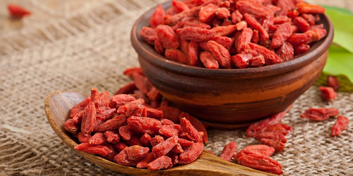 Bowl and spoon filled with dried goji berries on burlap.